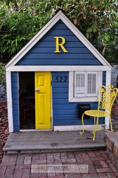 a small blue and white house with a yellow chair next to it on a brick walkway