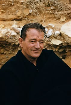 a man sitting in front of a stone wall