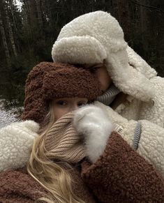 a woman with long hair wearing a brown and white coat in the snow, covering her face