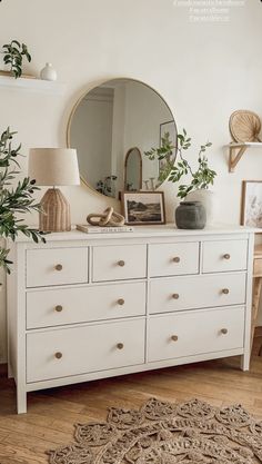 a white dresser topped with lots of drawers next to a mirror and potted plant