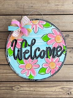 a welcome sign hanging on the side of a wooden wall with pink and green flowers