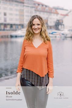 a woman standing in front of a body of water wearing an orange top and black pants