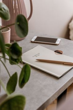 a table with a phone, pen and notebook on it next to a pink vase