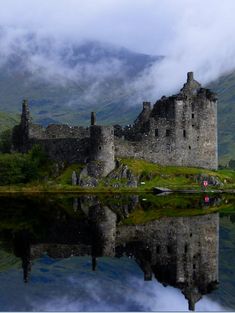 an old castle sitting on top of a green hill next to a body of water