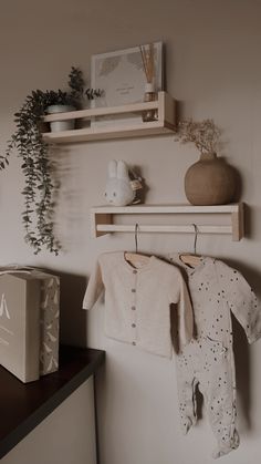 a baby's clothes hanging on the wall next to a box and some plants