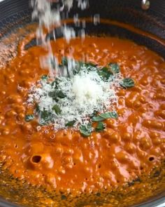 someone sprinkling parmesan cheese on top of a bowl of red sauce