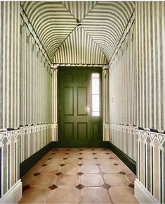 an empty hallway with tiled floors and green door leading to another room that has striped walls