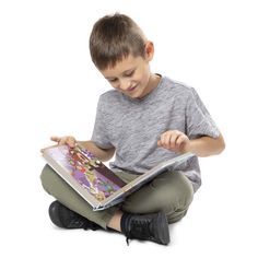 a young boy sitting on the floor reading a book with his hands in front of him