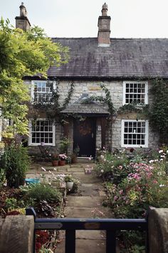 an old stone house with lots of flowers in the front and side windows on both sides