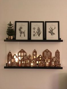 three framed pictures on a wall above a shelf filled with gingerbread houses and lit candles