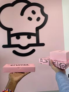 a person holding up some pink boxes in front of a wall