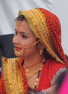 a woman in an orange and yellow outfit with jewelry on her head, looking to the side