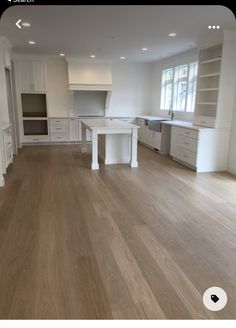 an empty kitchen with wooden floors and white cabinets in the center is seen from across the room