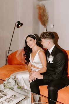 a bride and groom sitting on an orange couch