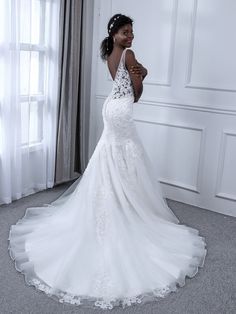 a woman in a white wedding dress standing next to a window