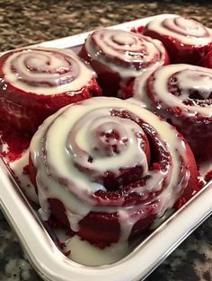 some red velvet rolls are sitting in a white dish on a counter top and drizzled with icing