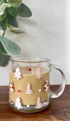 a glass mug filled with coffee sitting on top of a wooden table next to a potted plant