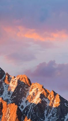 the mountains are covered in snow and pink clouds at sunset or sunrise, as seen from below