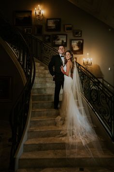 a bride and groom standing on the stairs at their wedding reception in front of chandeliers