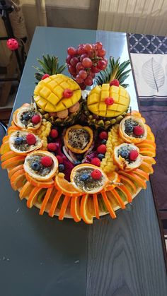 an arrangement of fruit is arranged on a table with grapes, pineapples and oranges