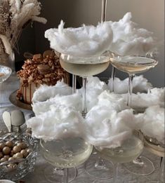 several glasses filled with white liquid and cotton flakes on top of a table next to desserts