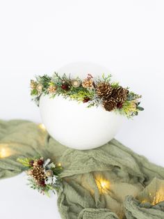 a white vase with pine cones and greenery in it sitting on a green scarf