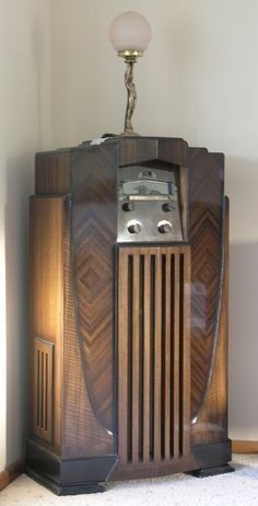 an old fashioned radio sitting on top of a wooden cabinet next to a wall lamp