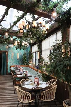 an outdoor dining area with wicker chairs and tables covered in plants, hanging lights and potted trees