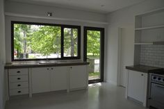 an empty kitchen with large windows and white cupboards on either side of the counter