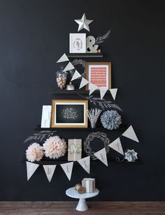 a christmas tree decorated with white and pink decorations on top of a wooden table in front of a black wall