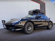 a black sports car is parked in front of a building with its luggage on the roof