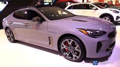 two cars are on display at an auto show, one is silver and the other is white