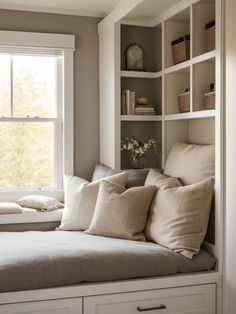 a window seat with some pillows on it in front of a bookshelf filled with books