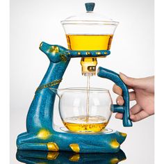 a person is pouring tea into a glass cup in front of a blue bird statue