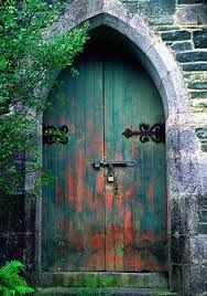 an old wooden door with wrought iron handles in front of a stone wall and tree