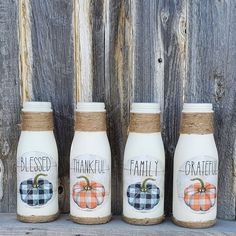 three jars with pumpkins painted on them are lined up in front of a wooden fence