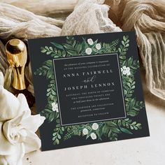 the wedding stationery is surrounded by white flowers and greenery, along with a gold spoon