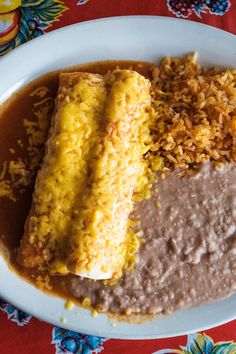 an enchilada, rice and beans on a white plate with a red table cloth