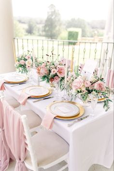 the table is set with pink flowers and gold place settings, along with white chairs