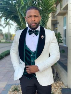 a man in a white tuxedo and green bow tie standing next to a palm tree