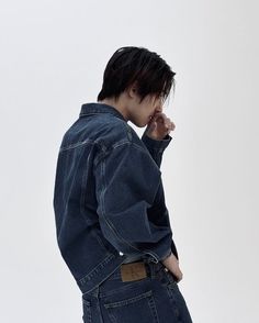 a young man wearing a jean jacket and jeans standing in front of a white wall