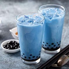 two glasses filled with blue liquid next to spoons