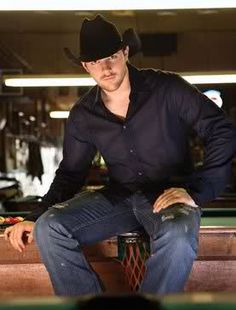 a man sitting on top of a pool table wearing a cowboy hat and holding a drink