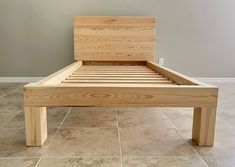 a wooden bed frame sitting on top of a tile floor next to a gray wall