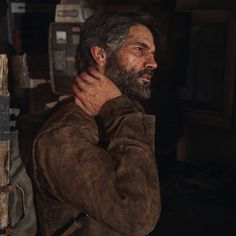 a man with a beard standing in front of a wall and holding his hand on his shoulder