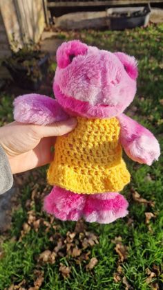 a pink and yellow teddy bear wearing a yellow dress in someone's hand on the grass