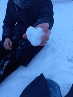 a person sitting in the snow holding up a heart shaped piece of white soap on their hand