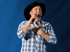 a man wearing a cowboy hat and holding a microphone up to his mouth while standing in front of a blue background