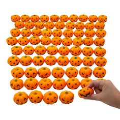 a hand is holding an assortment of orange pumpkins with faces on them and green dots in the middle