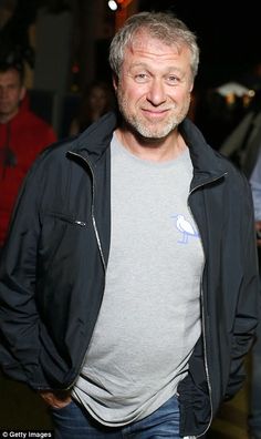 an older man with grey hair wearing a black jacket and blue jeans smiles at the camera